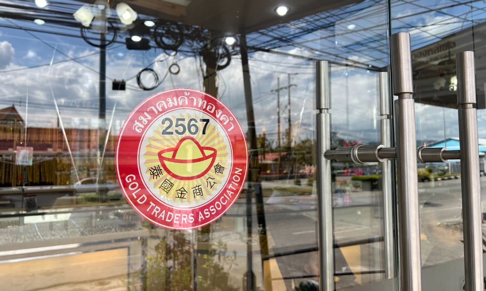  สติกเกอร์สีแดงและทองบนประตูกระจกที่มีตัวอักษรไทยและจีน บ่งบอกถึงการเป็นสมาชิกของสมาคมผู้ค้าทอง
