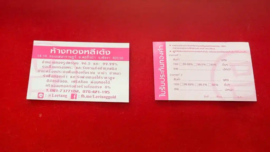 บัตรธุรกิจสองใบที่มีข้อความภาษาไทยถูกวางเรียงกันบนพื้นสีแดง; ใบหนึ่งแสดงข้อมูลติดต่อ ส่วนอีกใบมีแบบฟอร์มที่มีช่องกรอกข้อมูลและช่องทำเครื่องหมาย — รวมถึงรายละเอียดเกี่ยวกับแหวนทอง 1 กรัม ราคา และ ทอง 1 กรัม ราคาเท่าไหร่.