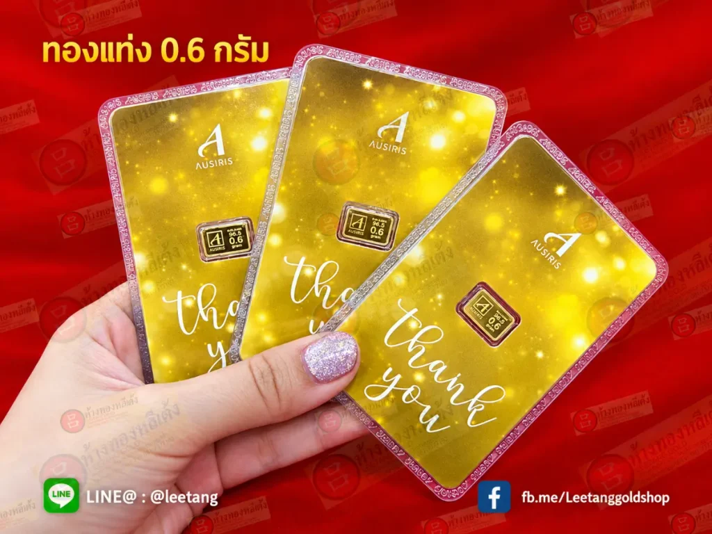 มือหนึ่งกำลังถือแท่งทอง Ausiris สามแท่ง แต่ละแท่งมีน้ำหนัก 0.6 กรัม และมีข้อความ “ขอบคุณ” บนบัตรทอง.